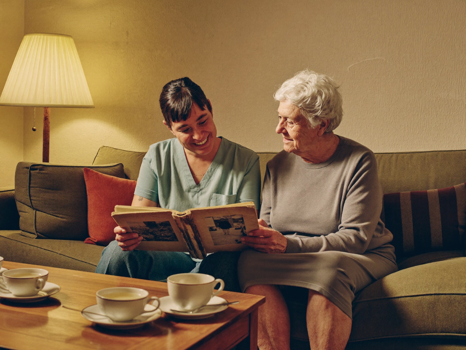 Betreuerin schaut gemeinsam mit einer Seniorin ein altes Fotoalbum an